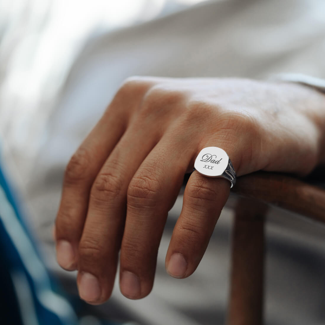 A man's hand wearing a sterling silver signet ring with the word Dad xxx engraved on it