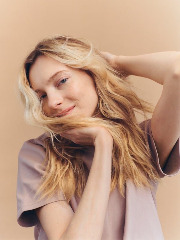 Woman with long, wavy blonde hair poses with chin in hand