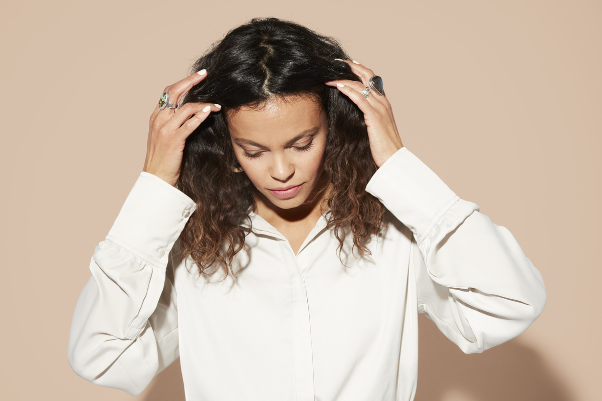 Woman looks down as she pushes back her middle-parted, wavy, long brown hair