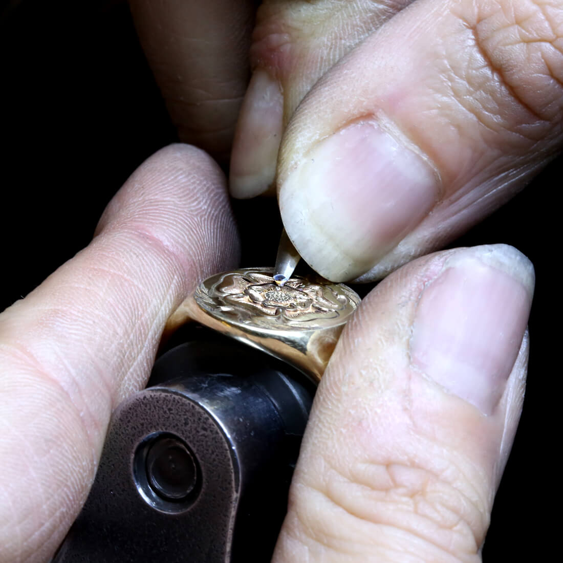 Jeweller's hands are engraving a rose using the technique of seal engraving o an oval yellow gold signet ring