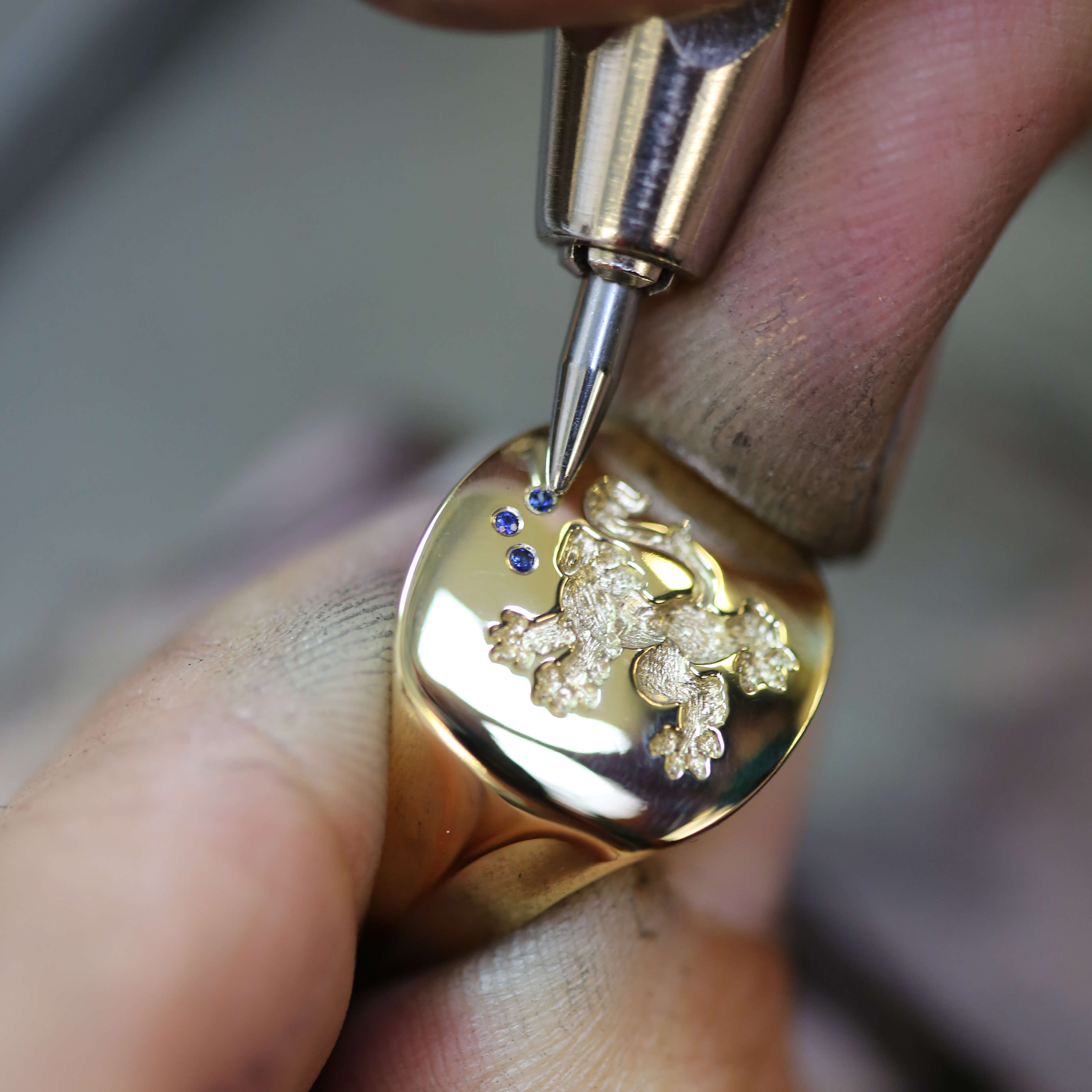 Male hands in a jewellery workshop setting blue sapphire stones on a gold signet ring with a dragon engraving using a sharp tool
