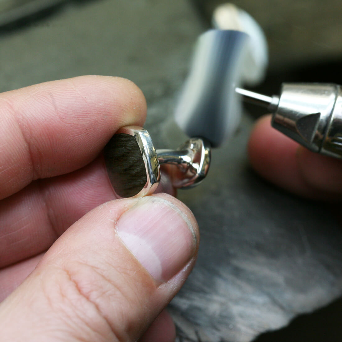 Our signet silver cufflinks with inlaid Thames wood at the top are being polished by a jeweller's hands in a workshop