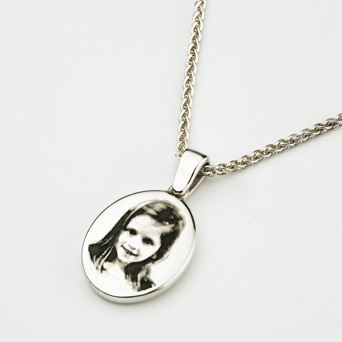 An oval signet necklace in silver with a little girl's face engraved on it in black and white