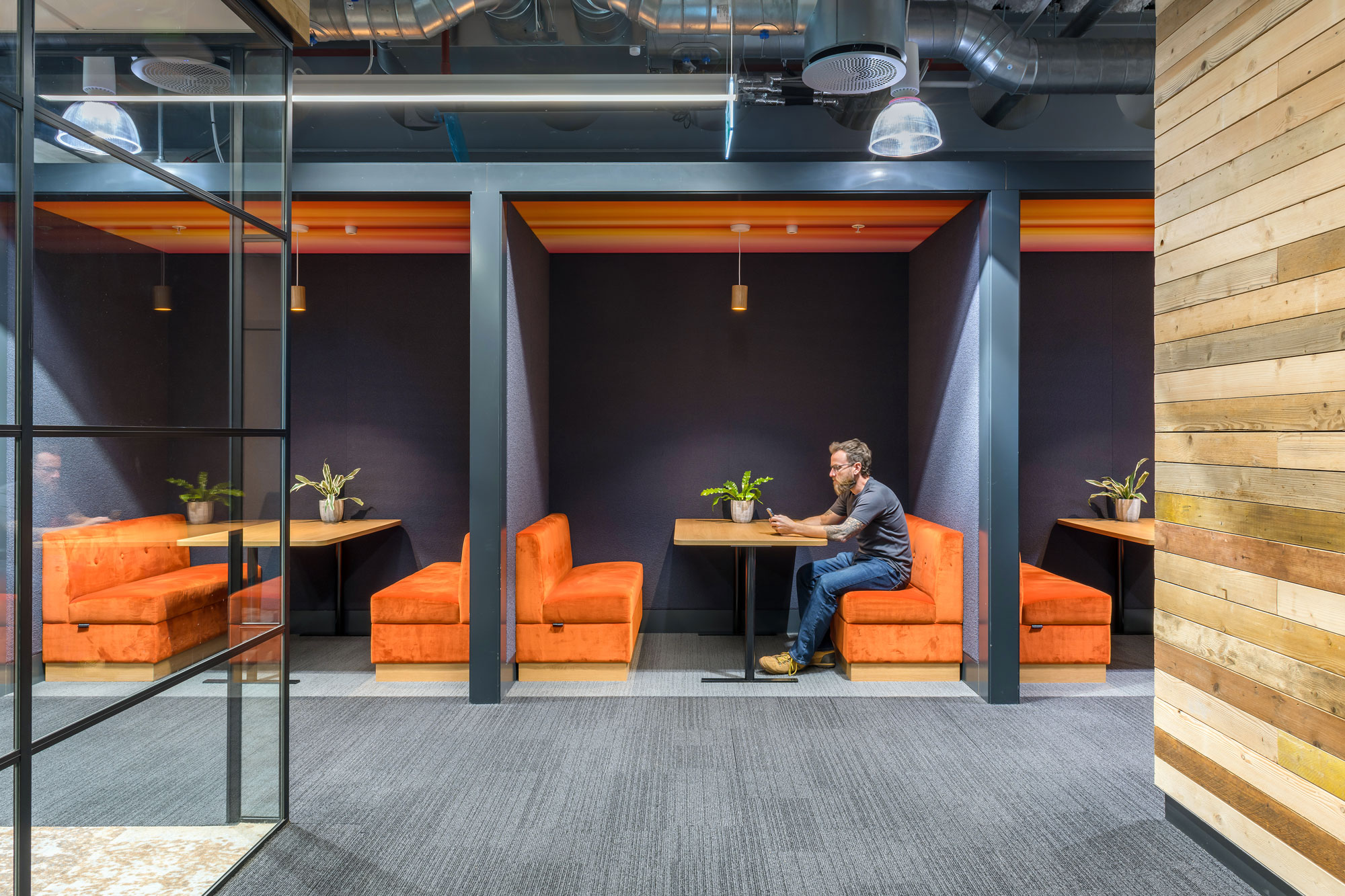 Person working on a laptop in a darkened work booth with bright orange sofas in Barclays office