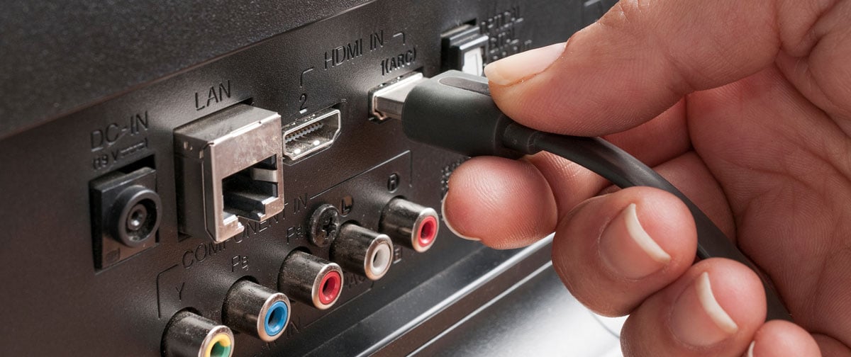 Hand plugging HDMI cable into the back of a television