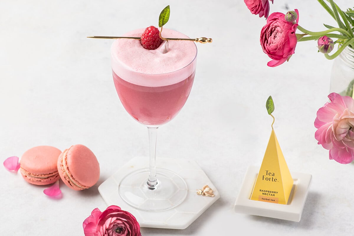 Raspberry Nectar Clover Club cocktail in a wine glass with pink cookies and roses