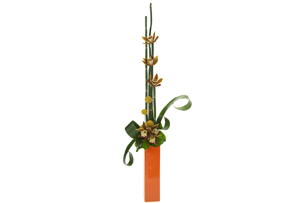 This beautiful linear floral design in a yellow orange color palette mixes mini-cymbidium orchids, billy balls, equisetum, aspidistra leaves, and galax leaves.