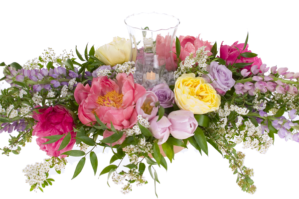 A soft and romantic wedding floral centerpiece mixes roses, peonies, lupine, tulips, spray roses, spirea, and Italian ruscus, then adds a glass hurricane with candle for an elegant effect.