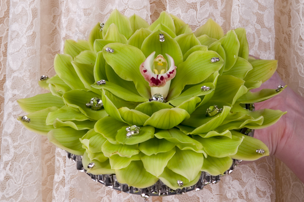 A magical bridal bouquet created from Cymbidium orchid blossoms has a perfect bloom in the middle, is enhanced with silver galax leaves, and adds crystals and rhinestones for bling.