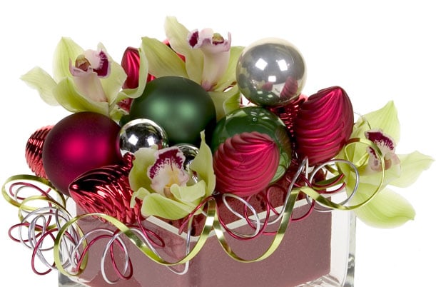 A holiday floral design mixes cymbidium orchid blooms with shiny Christmas ornaments and flat wire twisted into curlicues for a sparkling effect.