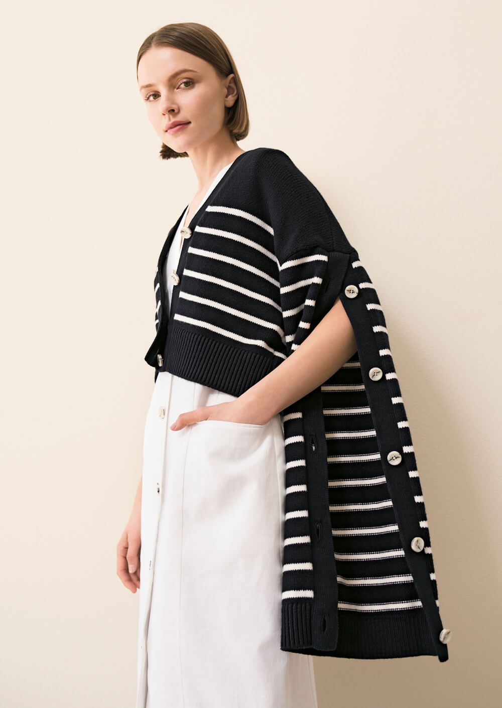 Model wears white trousers and a black and white striped knit sweater