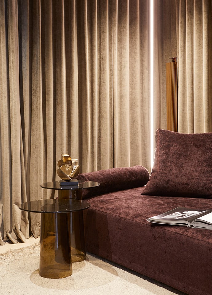 Plum-hued sofas and linear lighting create a moody, comfortable relaxation space that is ambient, serene and dramatic. Heavy velvet fabric curtains encompass the room in lush, dark folds.