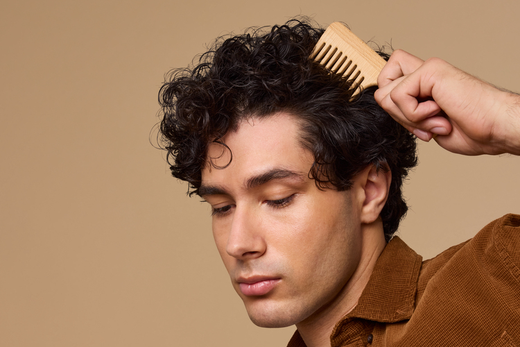 A person combs through their curly, pixie cut hair. 