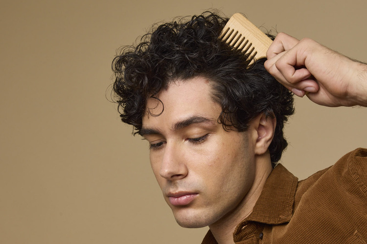 A person combs through their curly, pixie cut hair. 