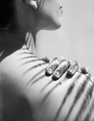 Schwarz-weißes Bild von einer Frau, das eine Schulter von hinten zeigt. 