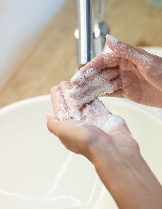 Zwei Hände mit schäumender Greek Yoghurt Waschcreme über einem Waschbecken. 