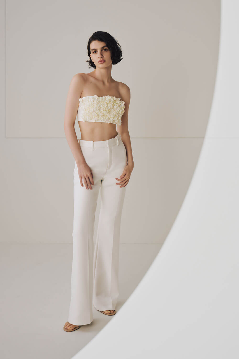 Model is wearing white pants and an off white floral tube top