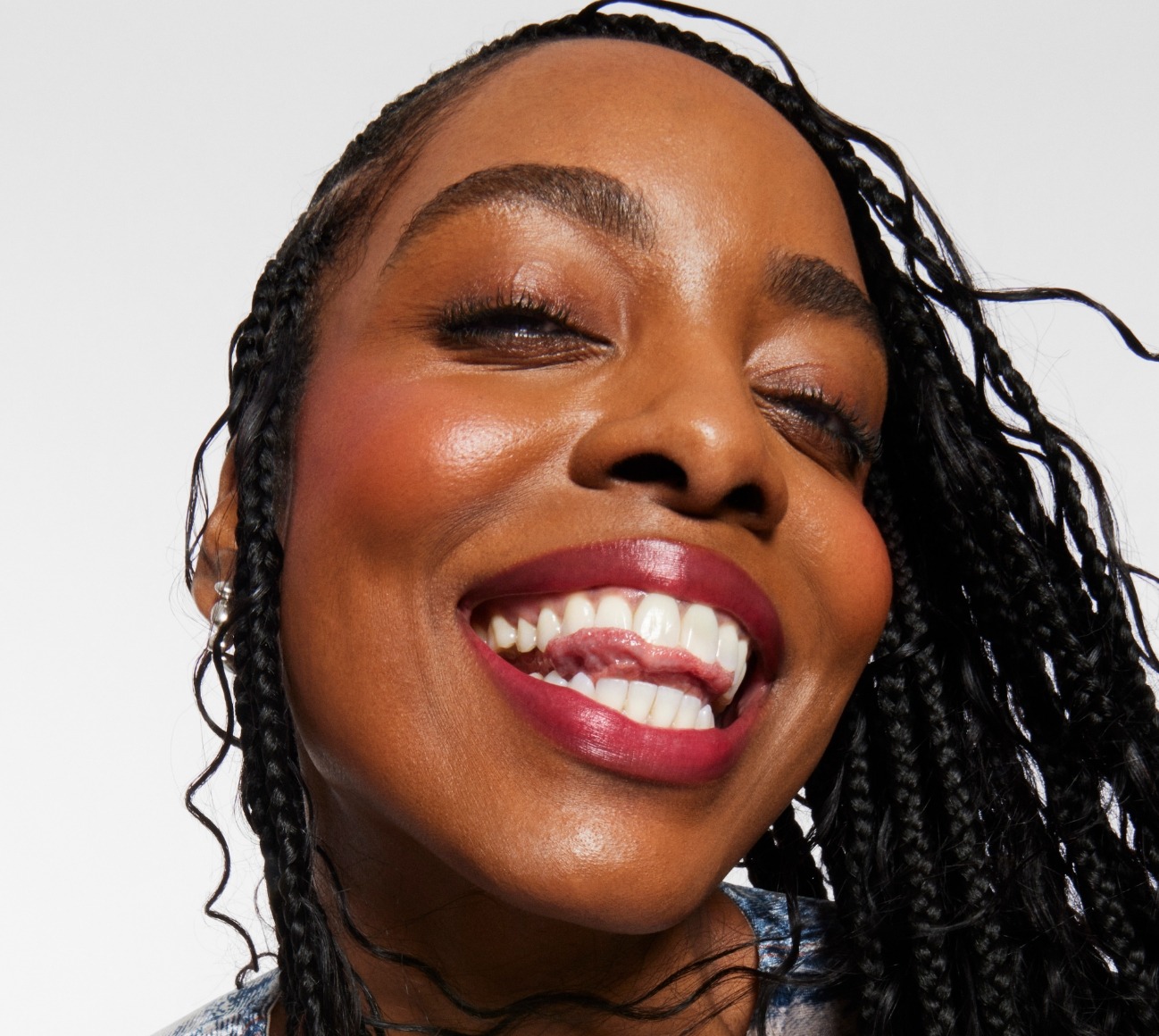 Smiling model wears a full face of Milk Makeup Products, including Hydro Grip Set + Refresh Spray against a light gray background
