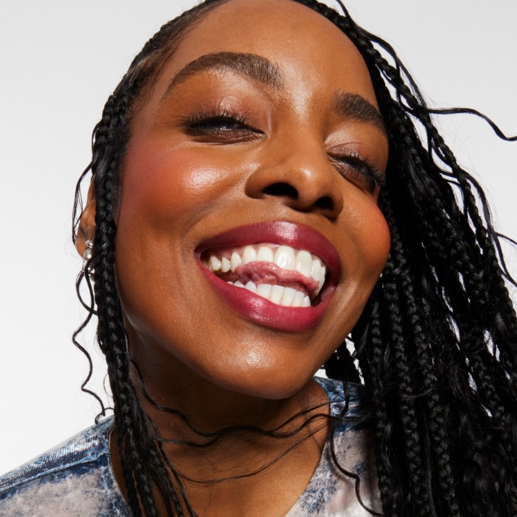 Smiling model wears a full face of Milk Makeup Products, including Hydro Grip Set + Refresh Spray against a light gray background