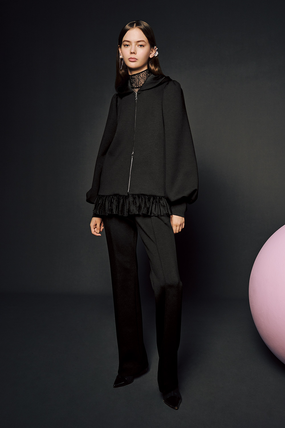 Model is wearing black pants and a black coat over a laced turtle neck top. 