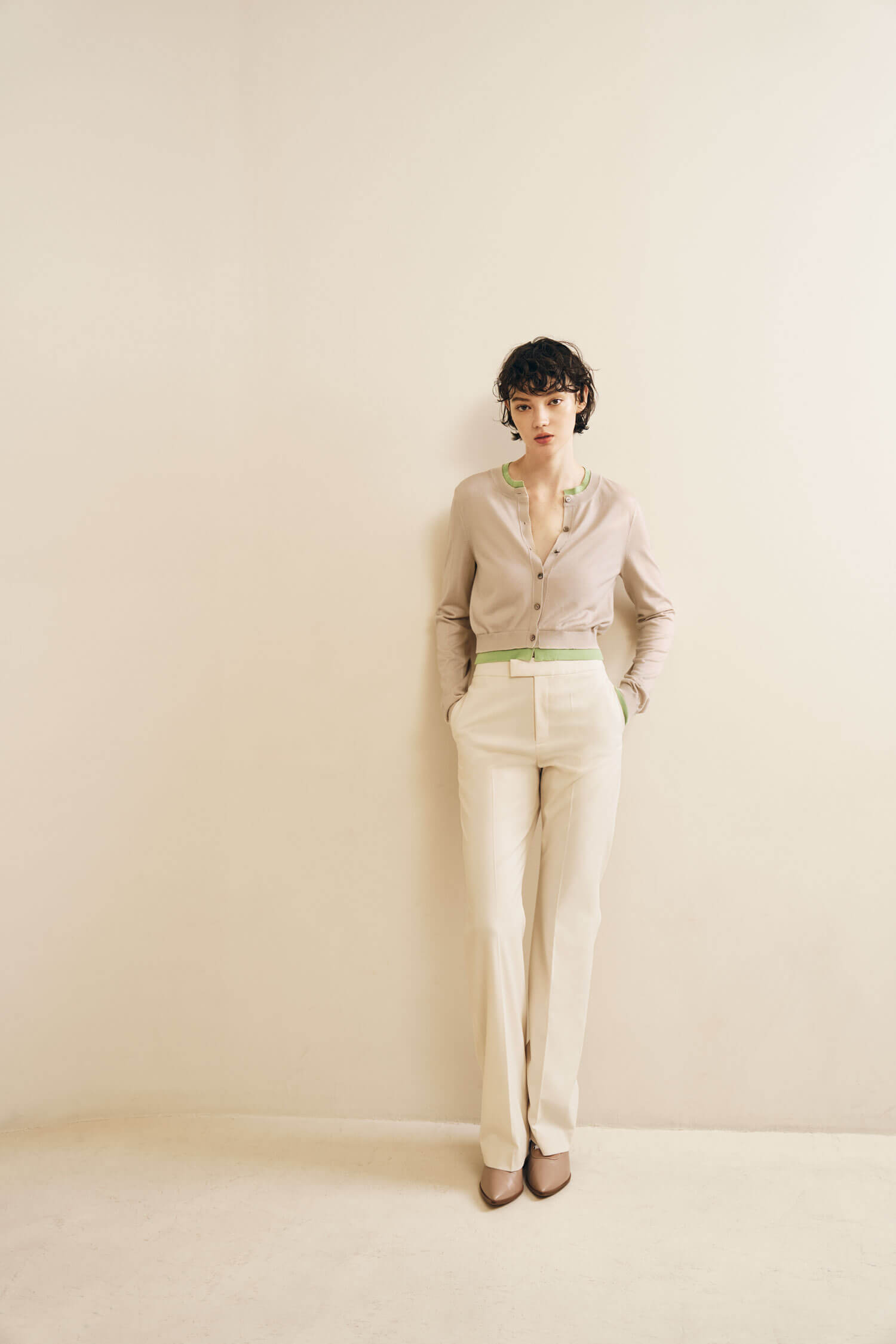 The model is wearing a light beige cardigan with green trim details, tucked into high-waisted cream trousers.