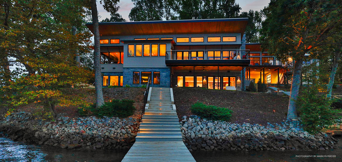 Dock and house on a lake with all the lights on inside the house