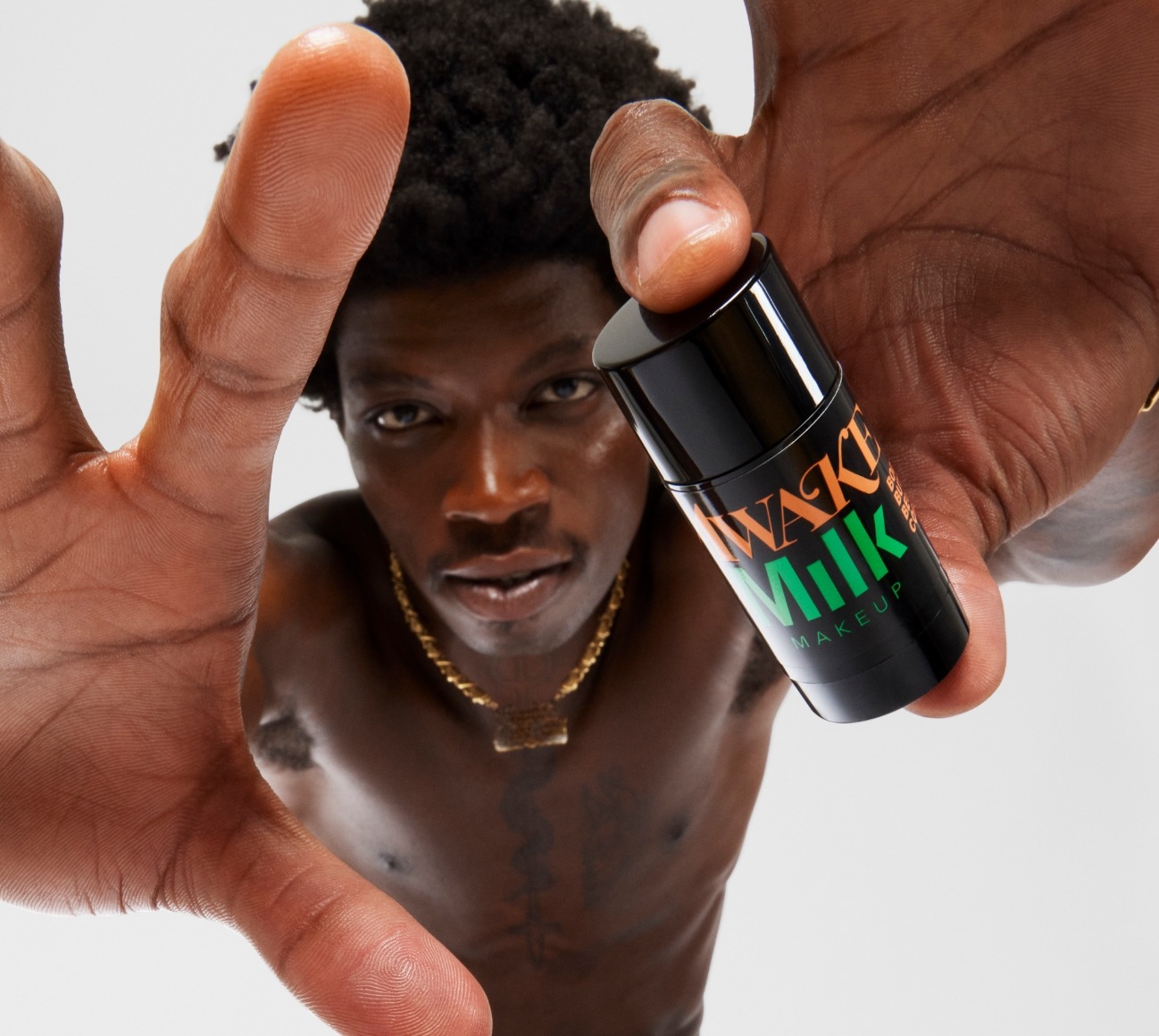 Close-up of model holding stick of Milk Makeup x Awake NY Body Butter on a white background