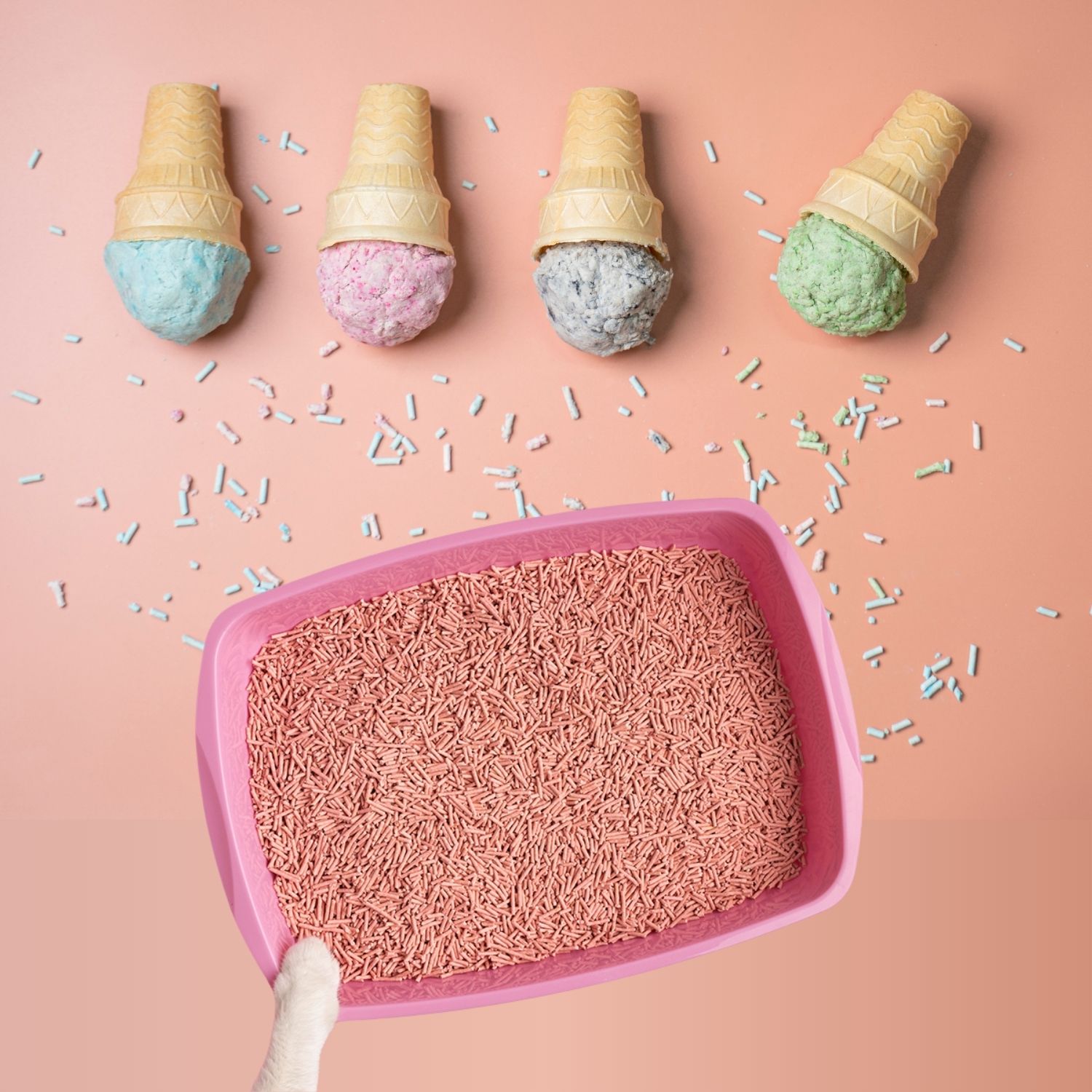 Four scoops of colourful cat litter shaped like ice cream cones sit above the tray on a peach background with scattered sprinkles.
