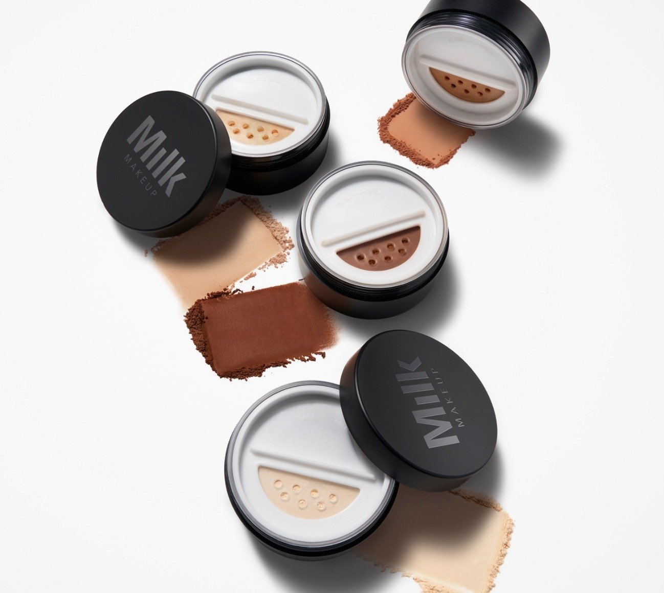 Product shot of four shades of Milk Makeup Pore Eclipse Matte Translucent Setting Powder next to a bit of the powder on a white background