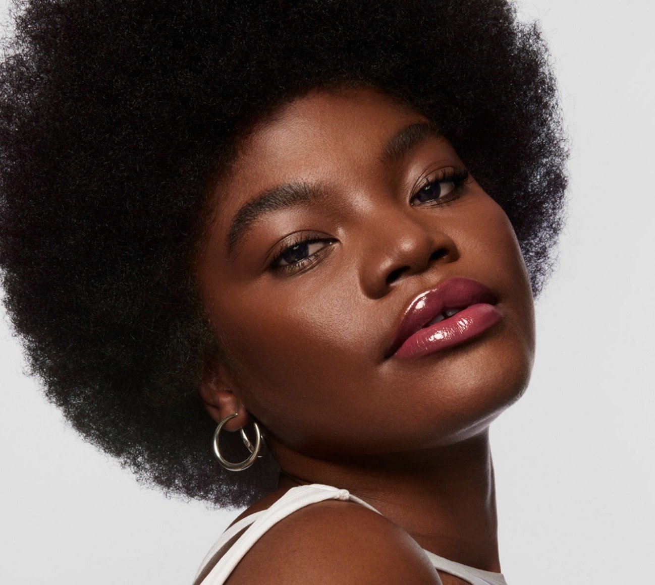 Model wears Milk Makeup Odyssey Lip Oil Gloss in Trek on a white background