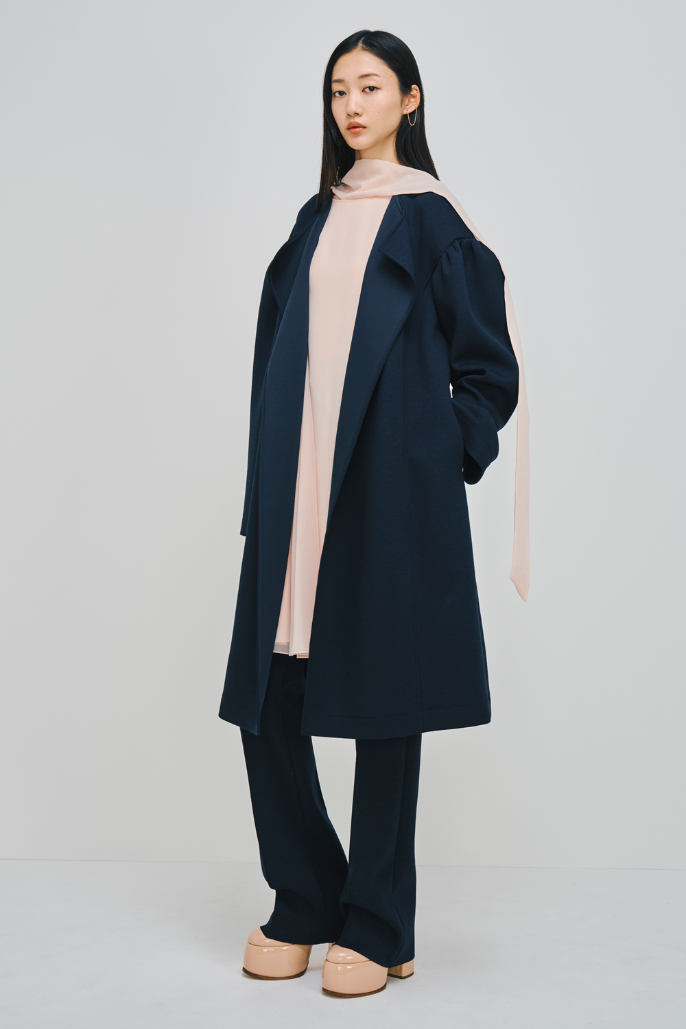 Model is wearing  navy pants and a matching coat over a pink top.