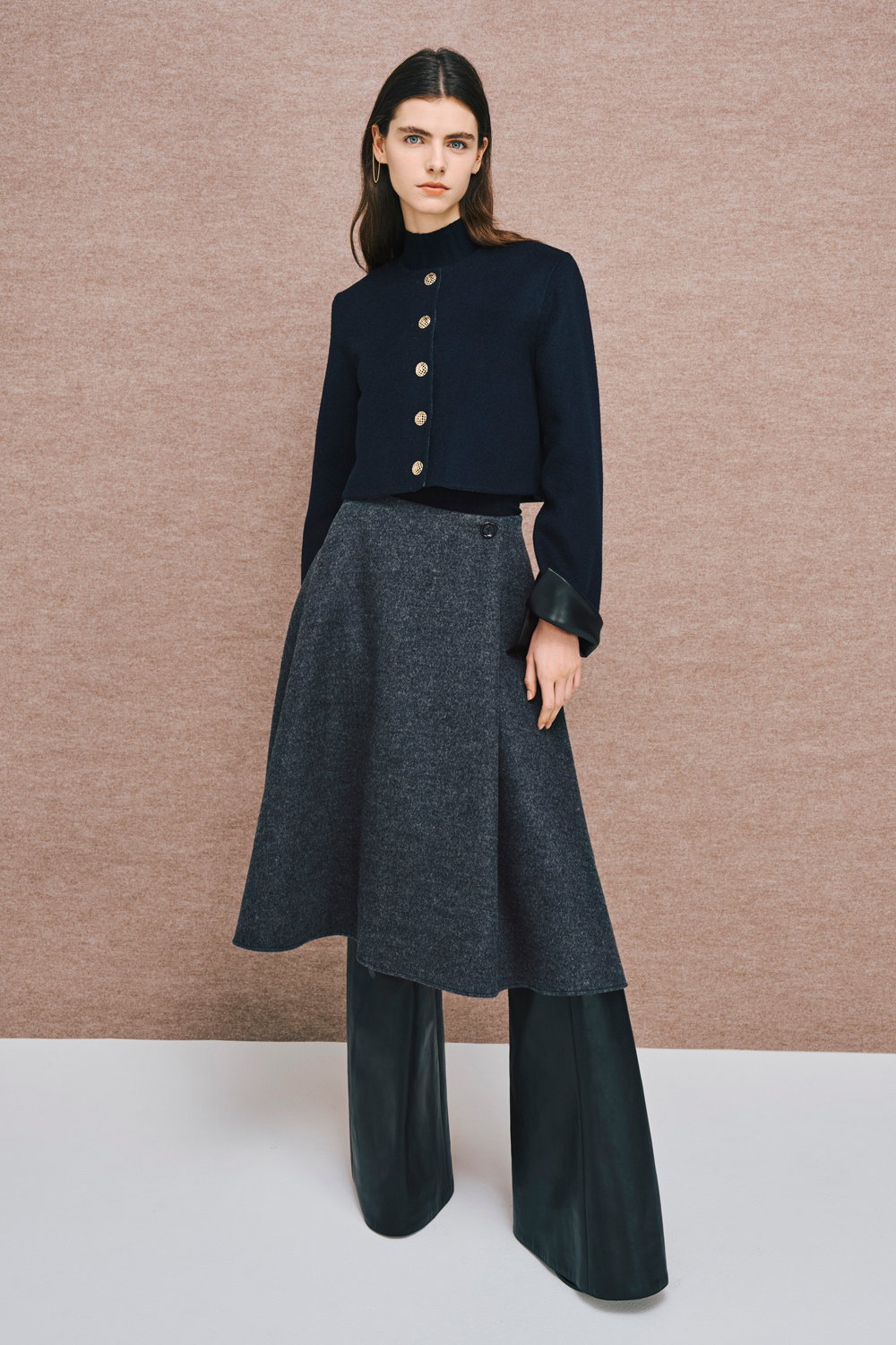 Model is wearing a gray skirt with a black short coat over a black top.