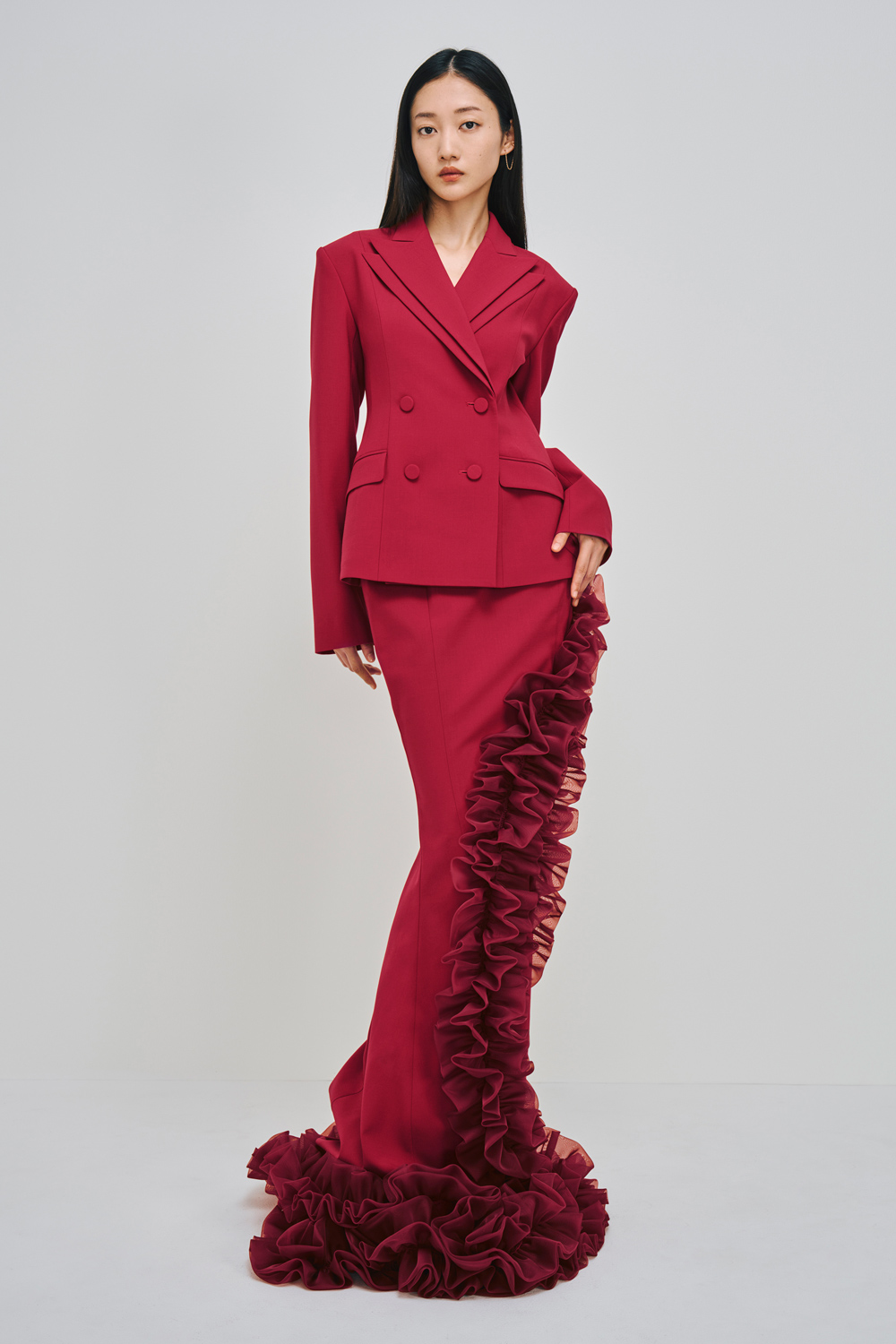 Model is wearing a red jacket and matching skirt with ruffle detailing.