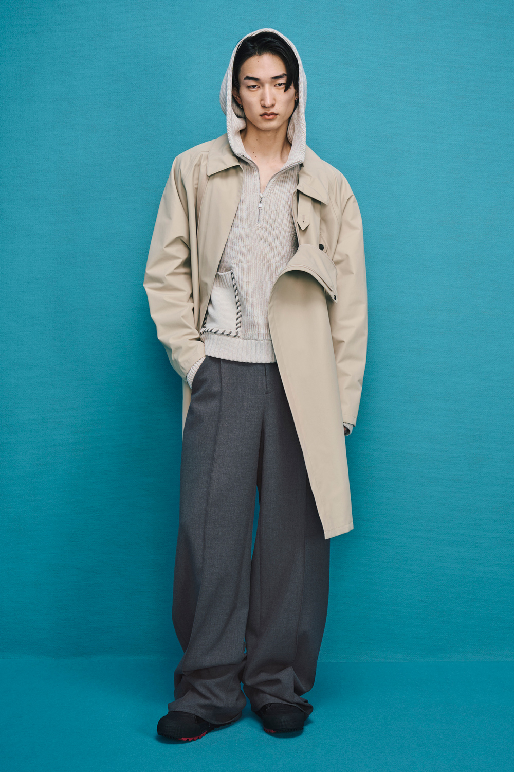 Model is wearing a gray pants with a beige coat over a beige hoodie.