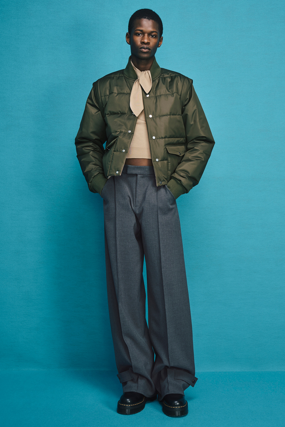 Model is wearing gray pants with a green jacket over a beige knit top.