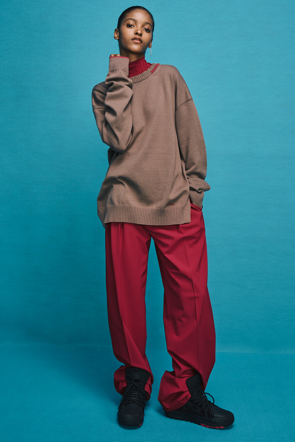 Model is wearing red pants with brown sweater over a red top.