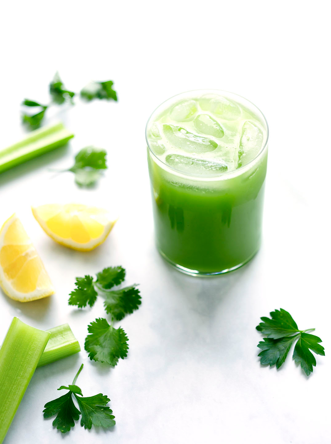 A glass of Green Herb Juice with celery, lemon, and parsley in the background