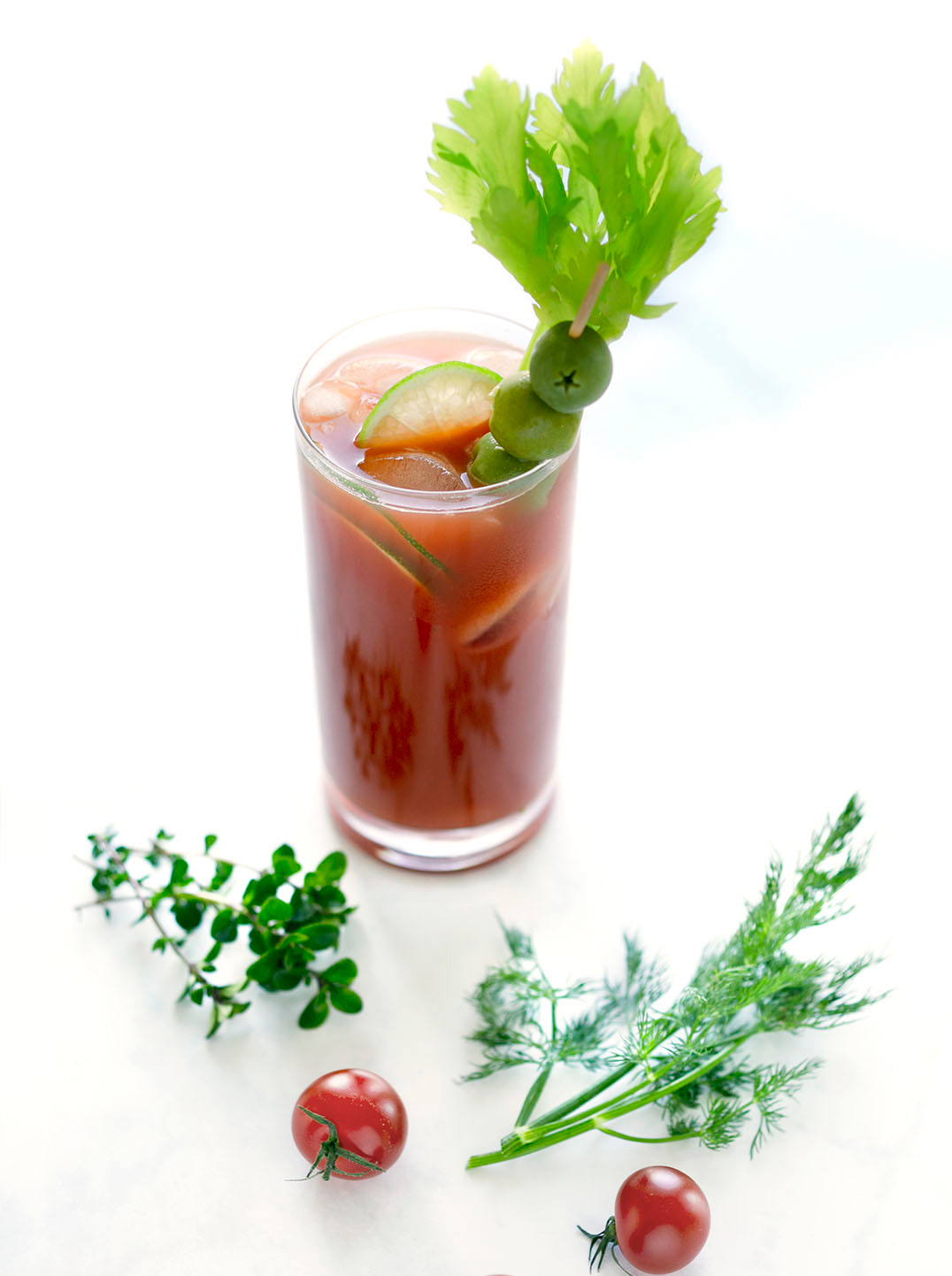 A deep red tomato based juice with ice and garnished with celery lime and a skewer of green olives