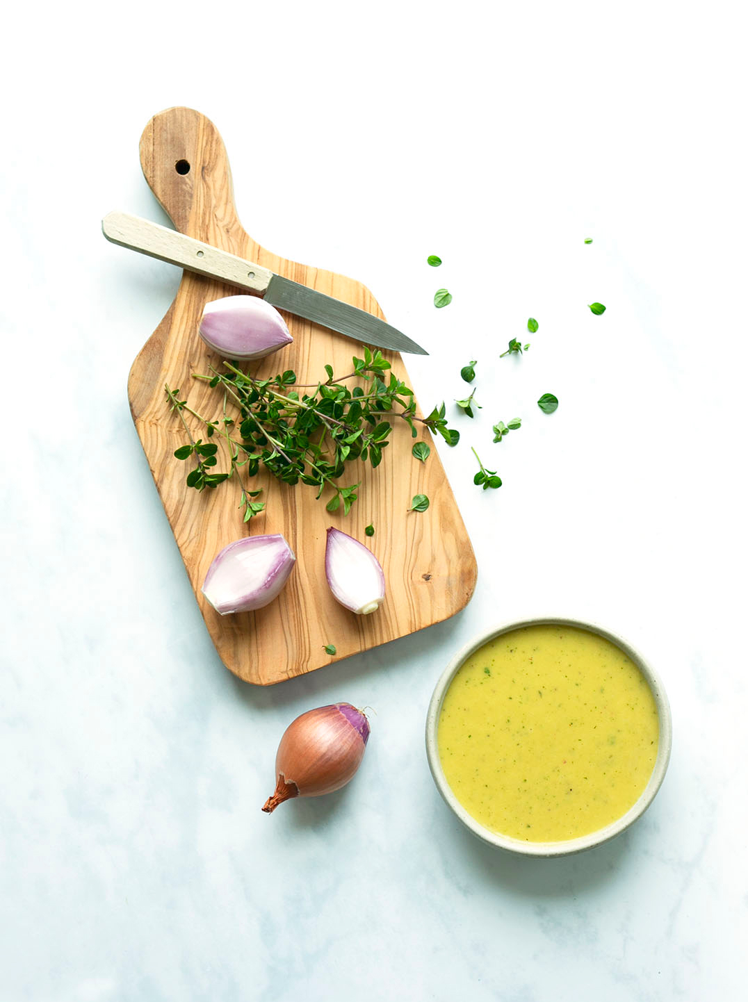 Overhead shot of a cutting board with herbs shallots and a small bowl of rich yellow herby shallot vinaigrette