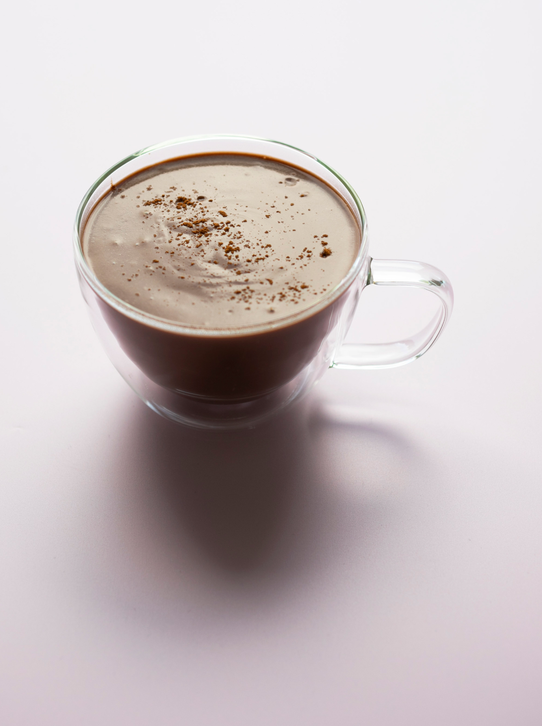 a glass cup with filled with a rich chocolatey spiced cacao milk on a pale taupe background 