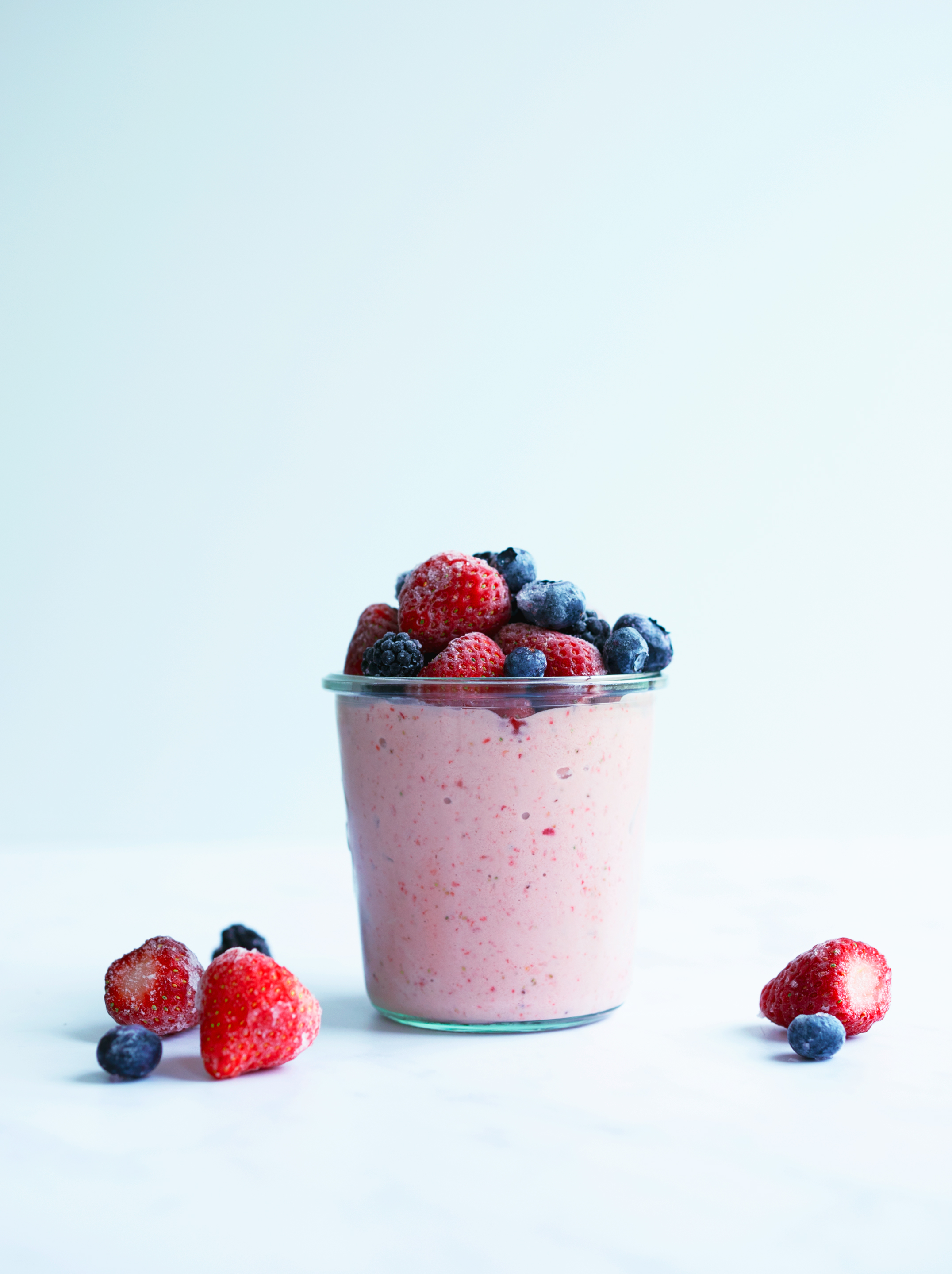 A glass of Strawberry Avocado Smoothie with strawberries and blueberries on top