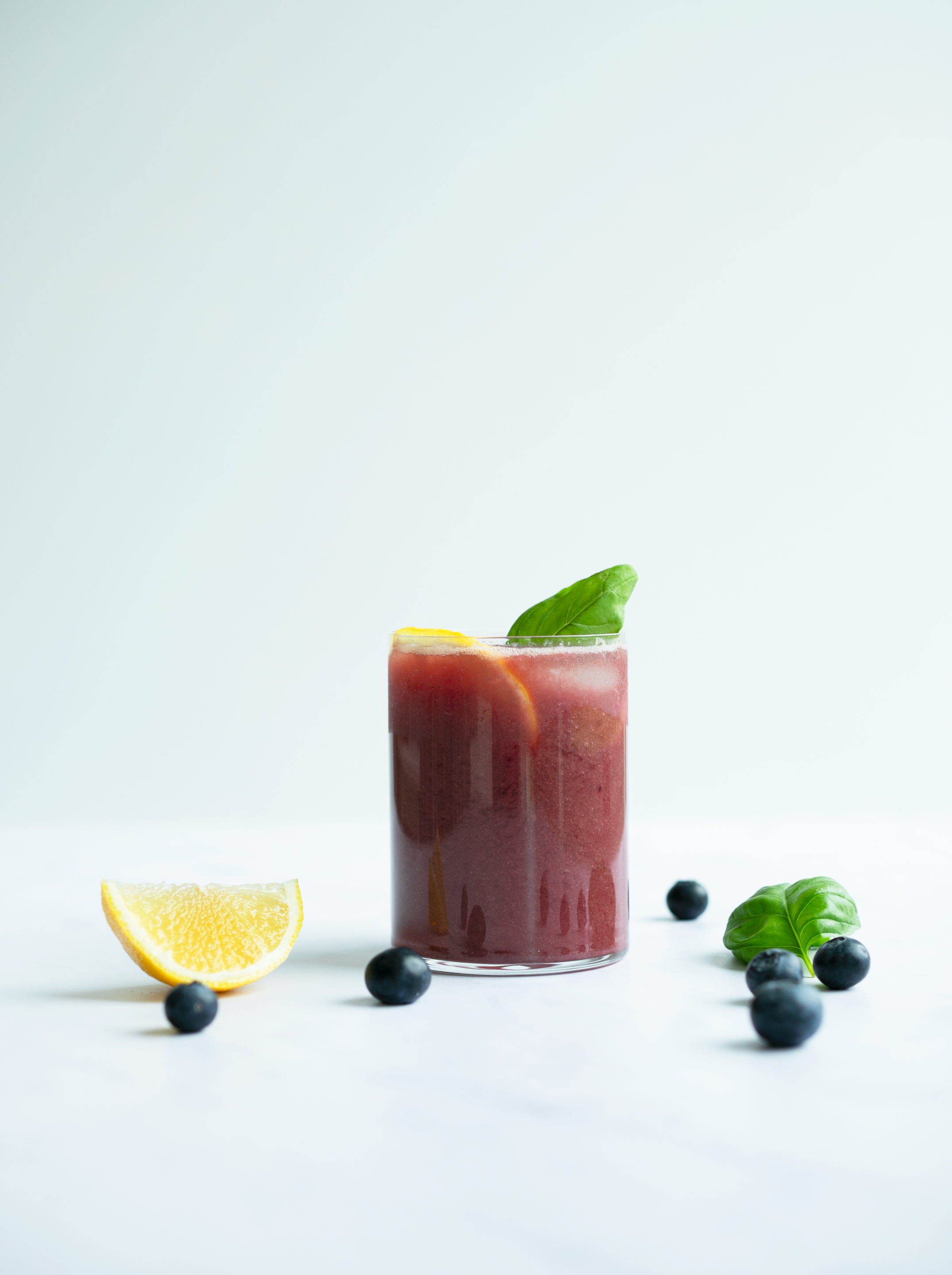 Glass of Blueberry Basil Lemonade with lemon wedge blueberry and mint in background