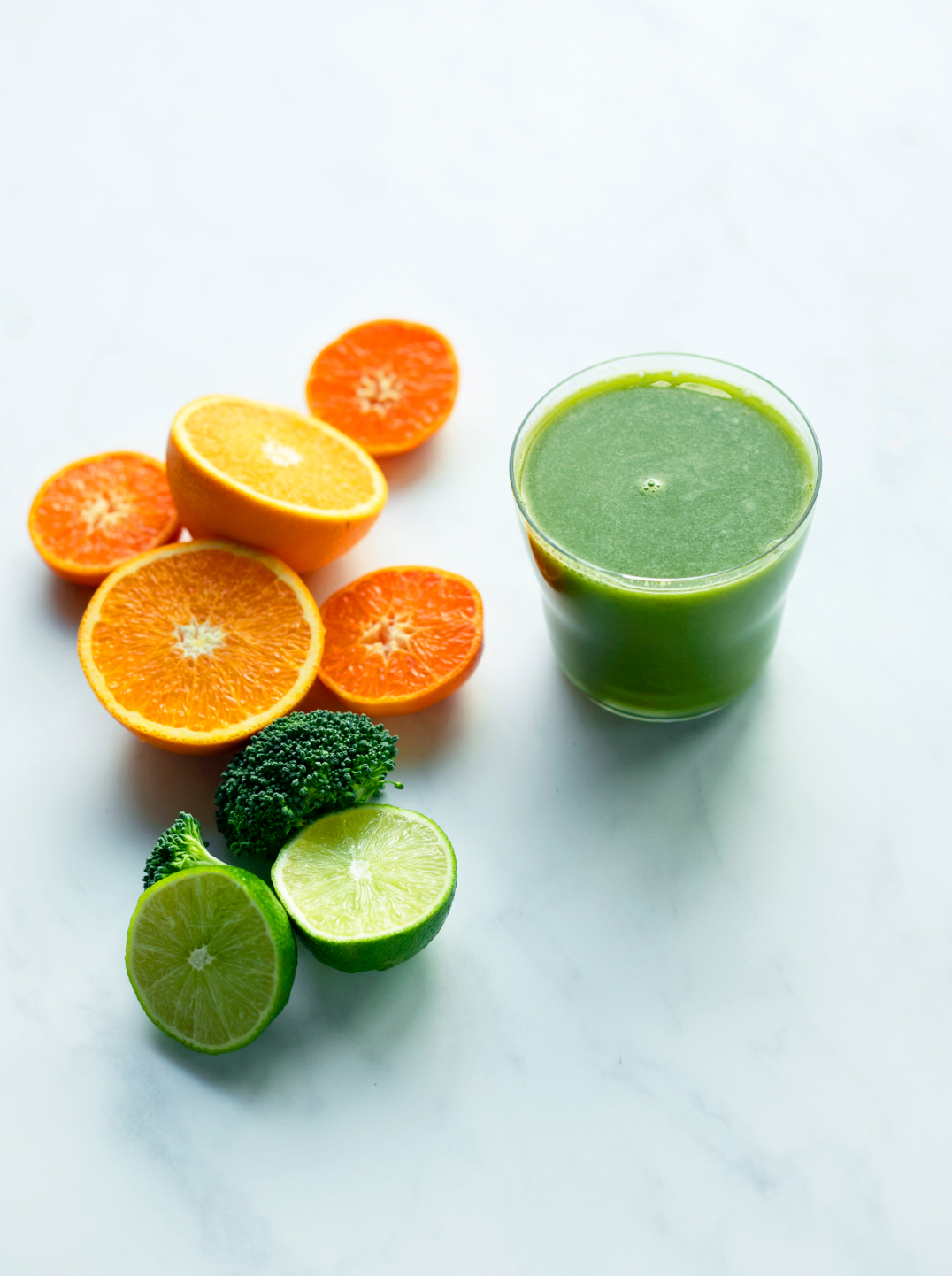 a glass green citrus glow juice with halved oranges and lime at left