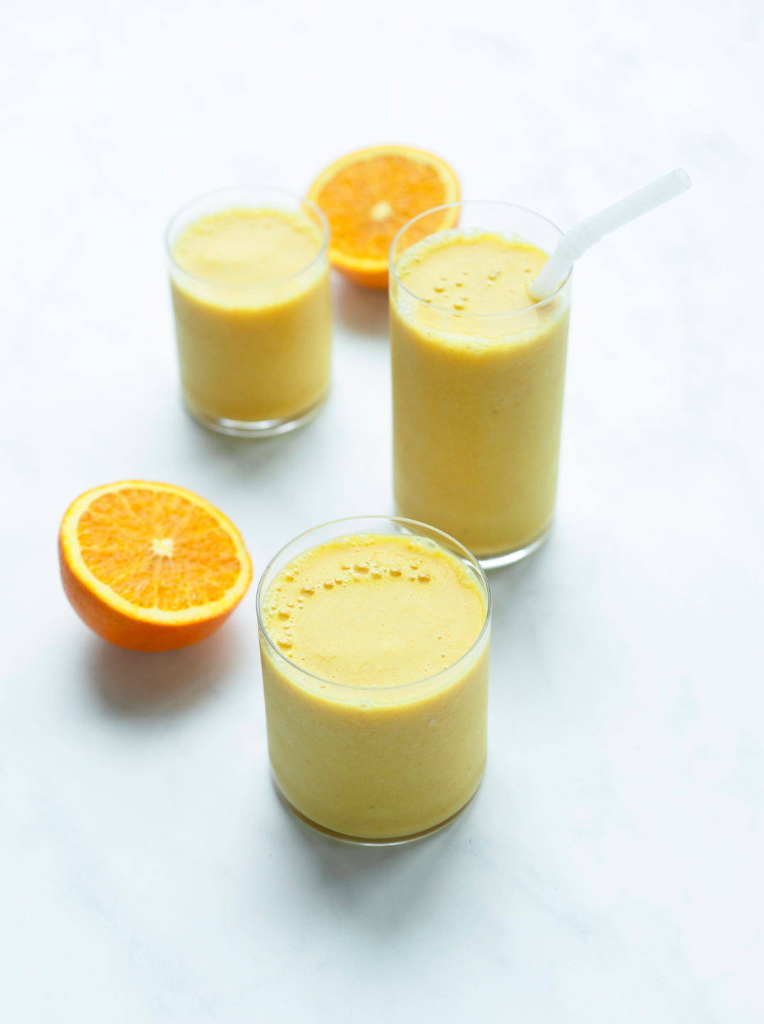 3 glasses of citrus sunrise smoothie with an orange cut in half