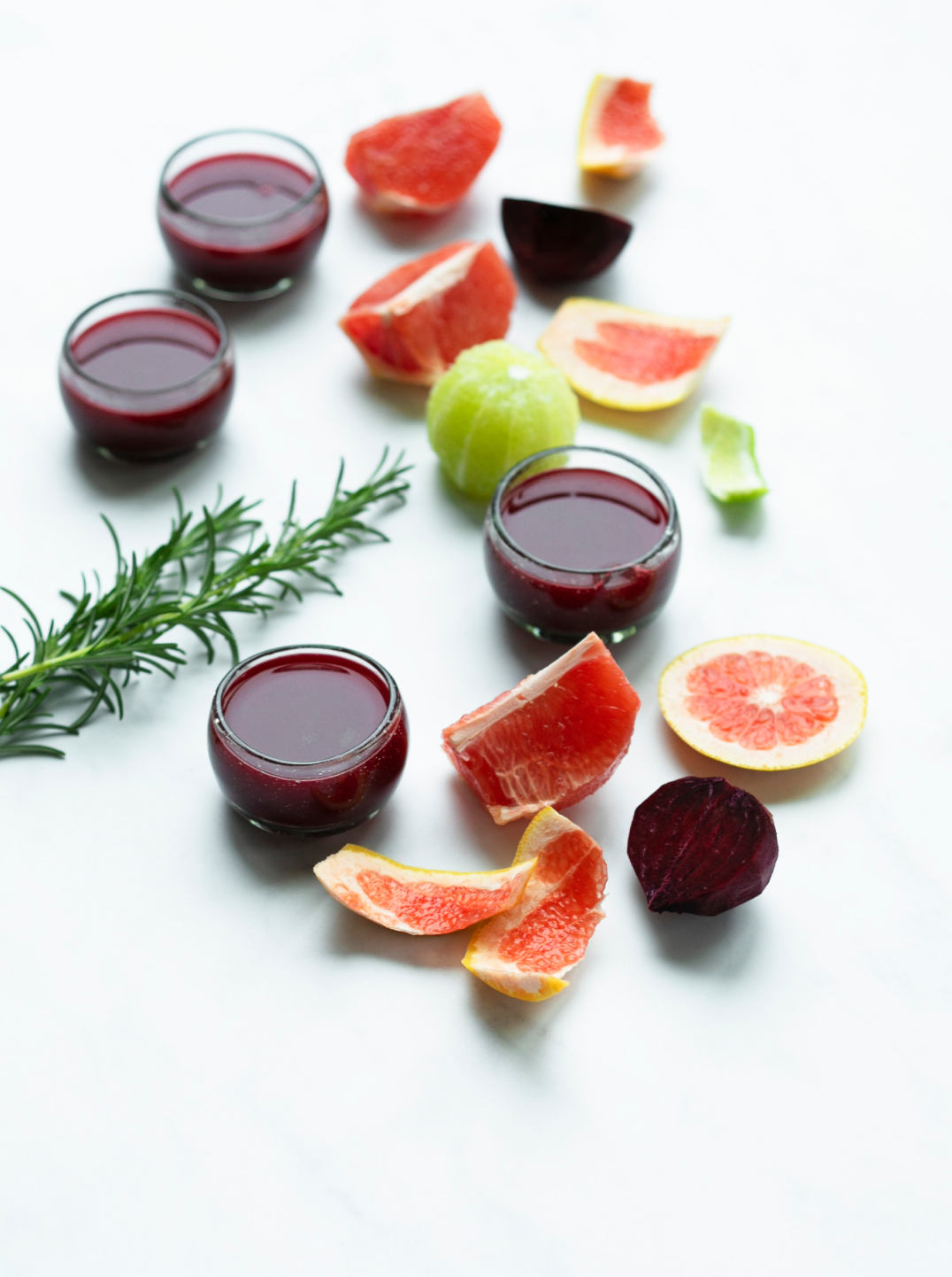 4 glasses of heart beet elixir surrounded by ingredients on a marble surface