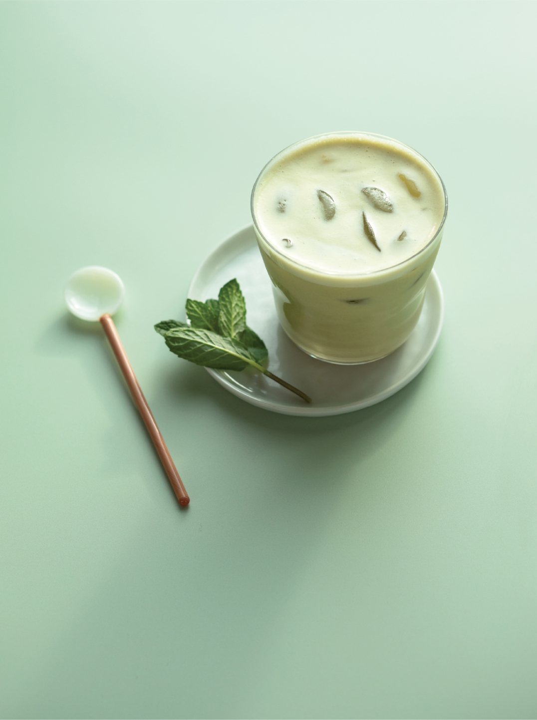 a glass of iced pistachio mint milk with a sprig of mint