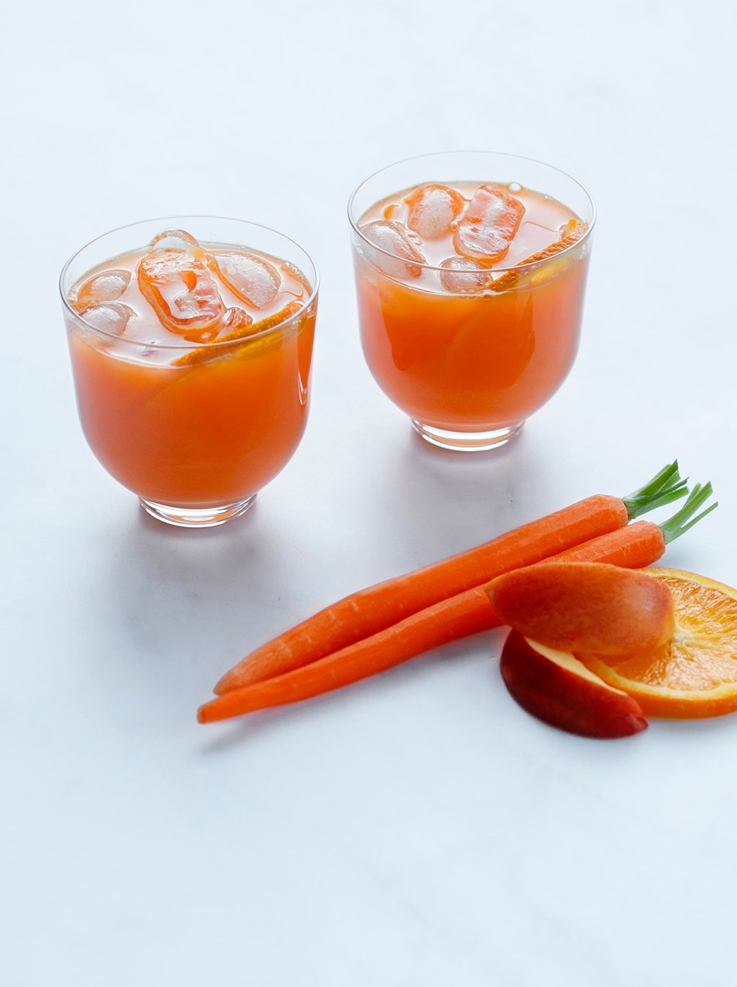 two glasses of orange appeal juice with carrots nectarine and orange slice
