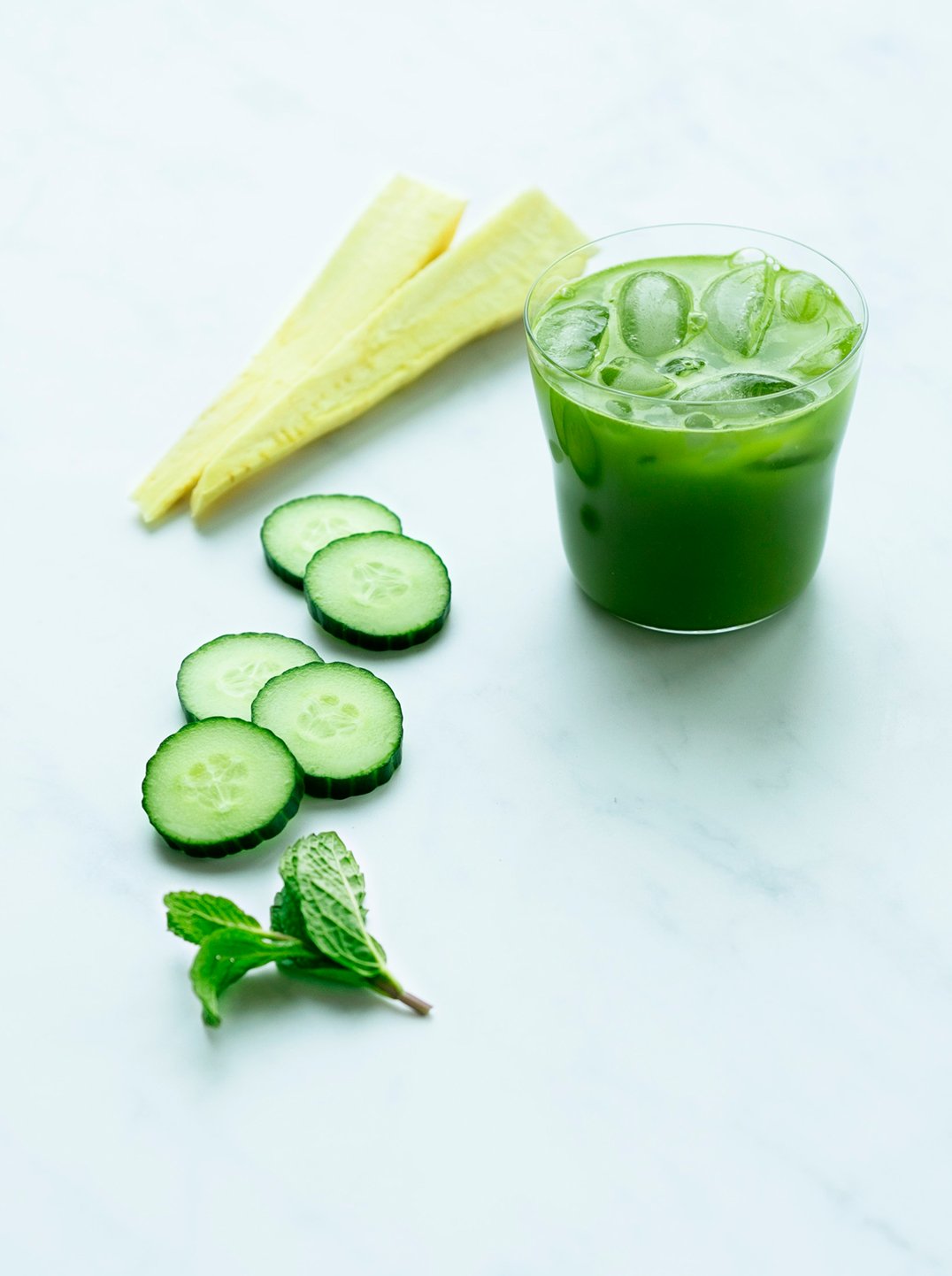 a glass of electric sunshine green juice iced with sliced parsnip cucumber and a sprig of mint
