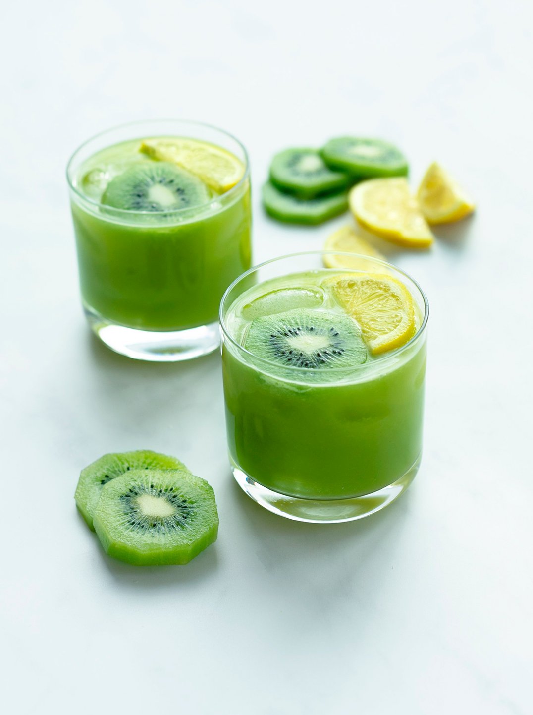 two glasses of go with your gut juice green juice garnished with kiwi and lemon