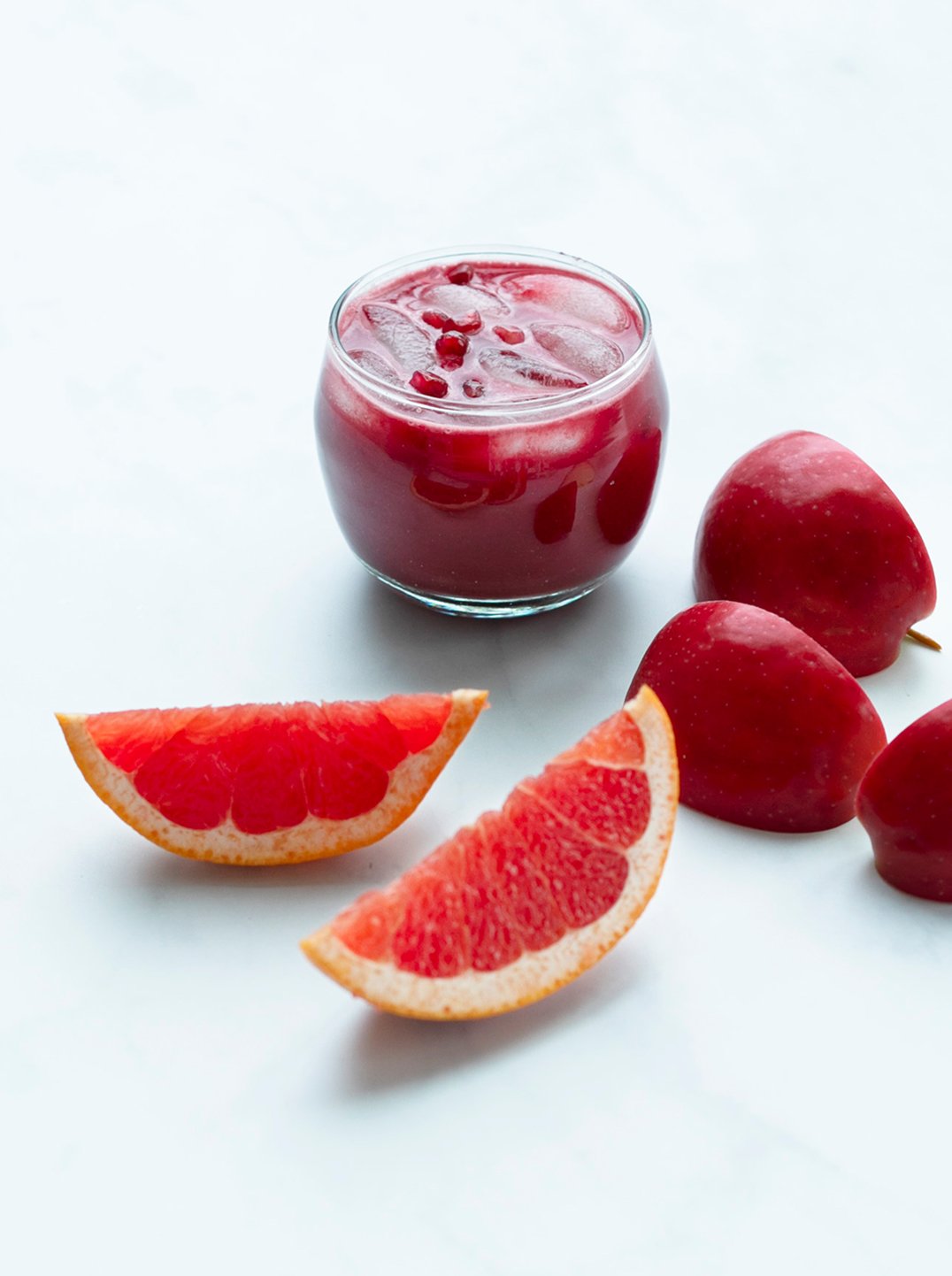 a glass filled with pom-beet brightener red juice with two blood orange wedges a cut beets